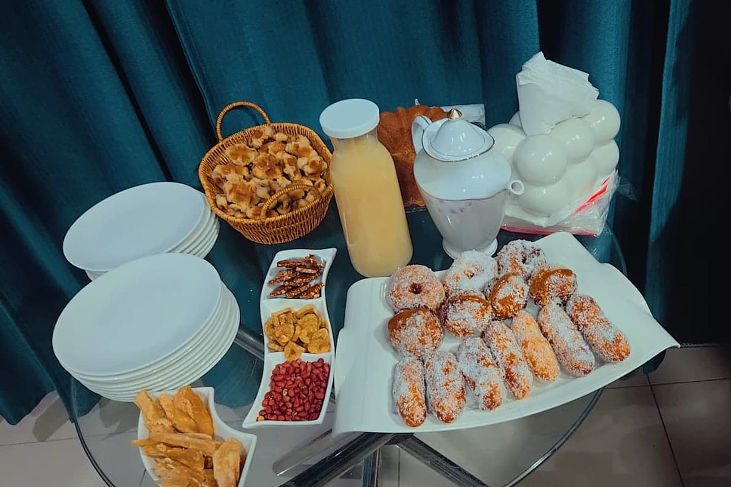 Mesa com sonhos de coco, bolachas, ginguba, banana frita, sumo natural e chá