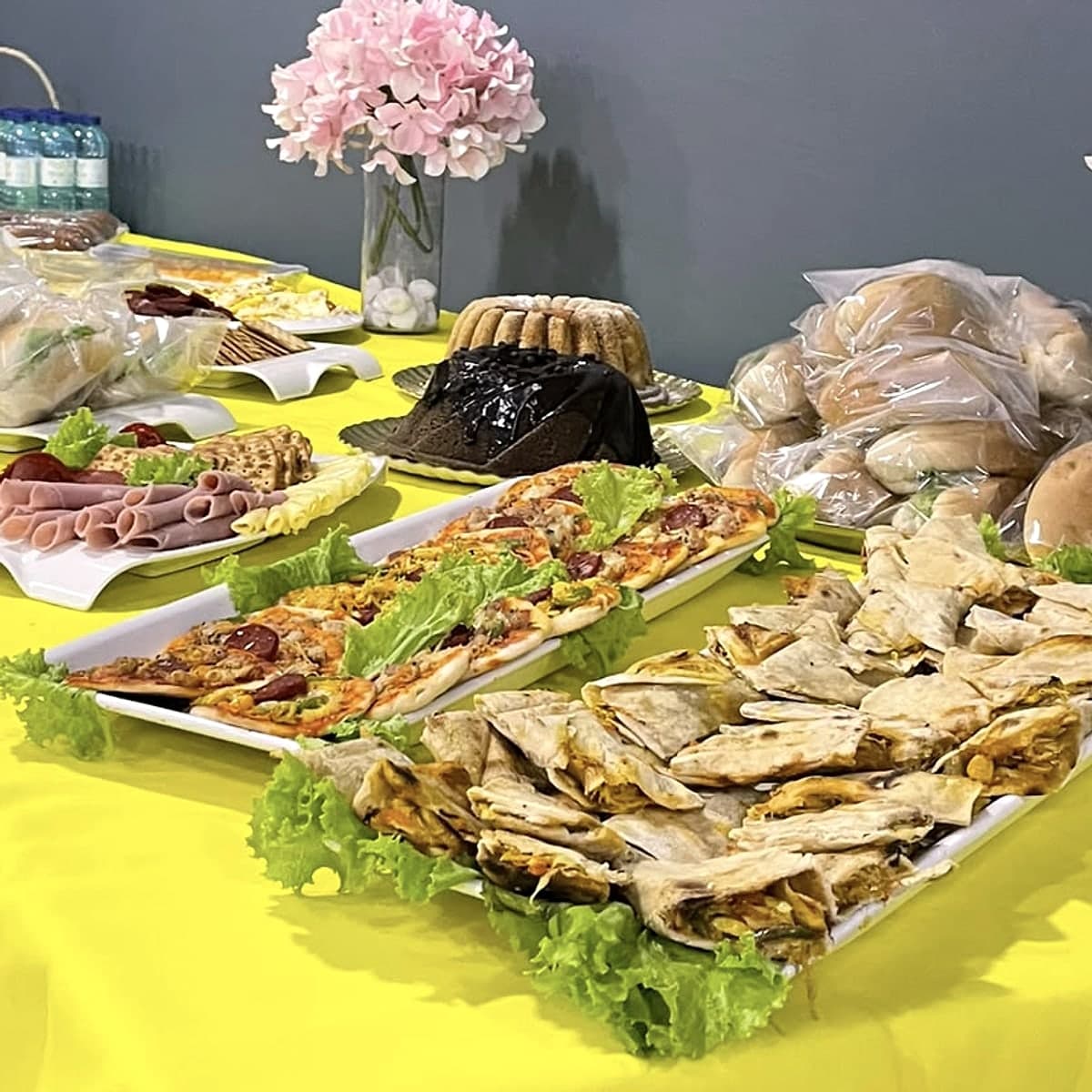 Mesa de coffee break com mini pizzas, wraps, frios, bolos e pães